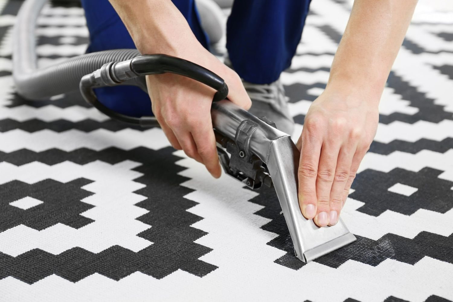 A person cleans a black and white carpet with a vacuum, highlighting a rug cleaning service in San Francisco, CA.