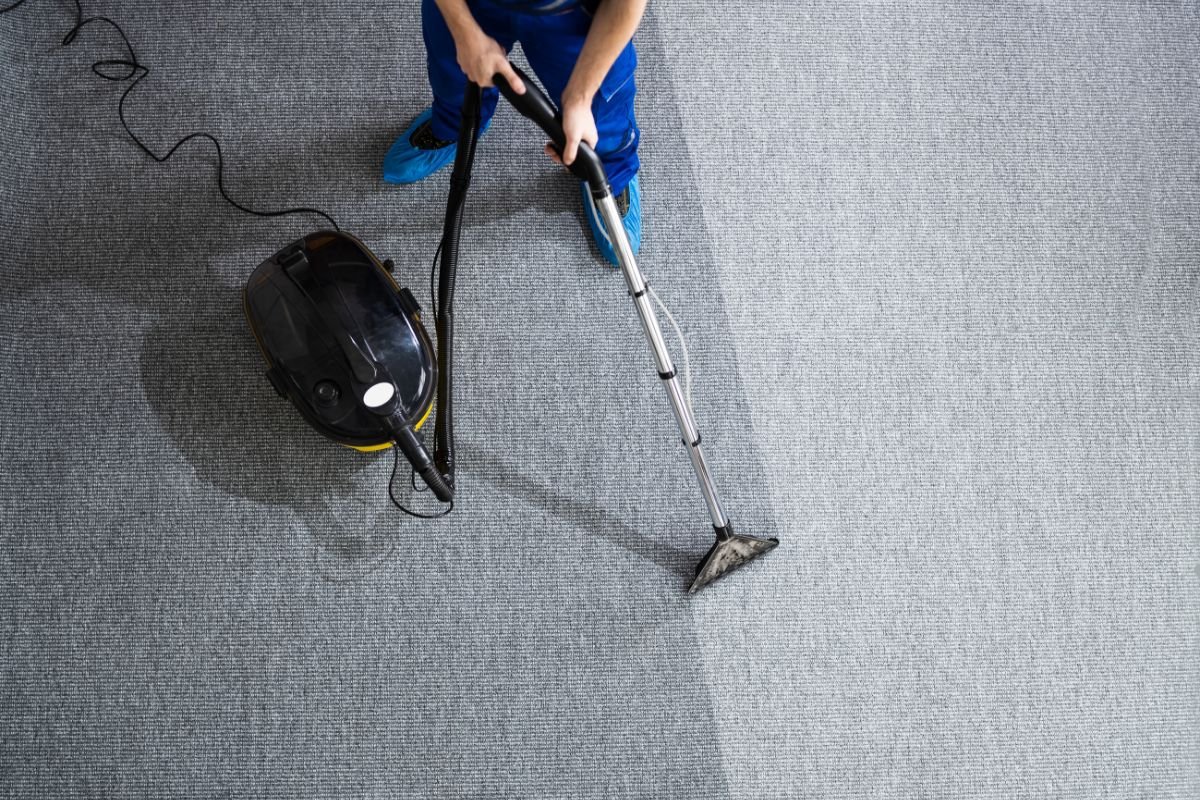 A person in blue overalls vacuuming a carpet, promoting Carpet Cleaning Solutions.
