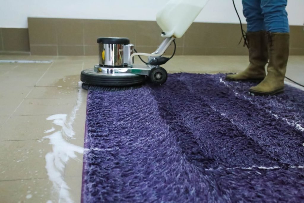 A person vacuums a purple rug, demonstrating a cleaning technique that includes vinegar in the carpet cleaner.